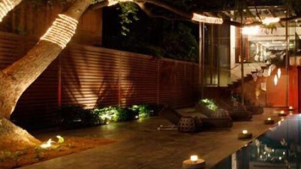 A nighttime view of a traditional Japanese-style garden with a wooden fence, a pathway, and a building with a red exterior. - The Park Pod (Chennai)