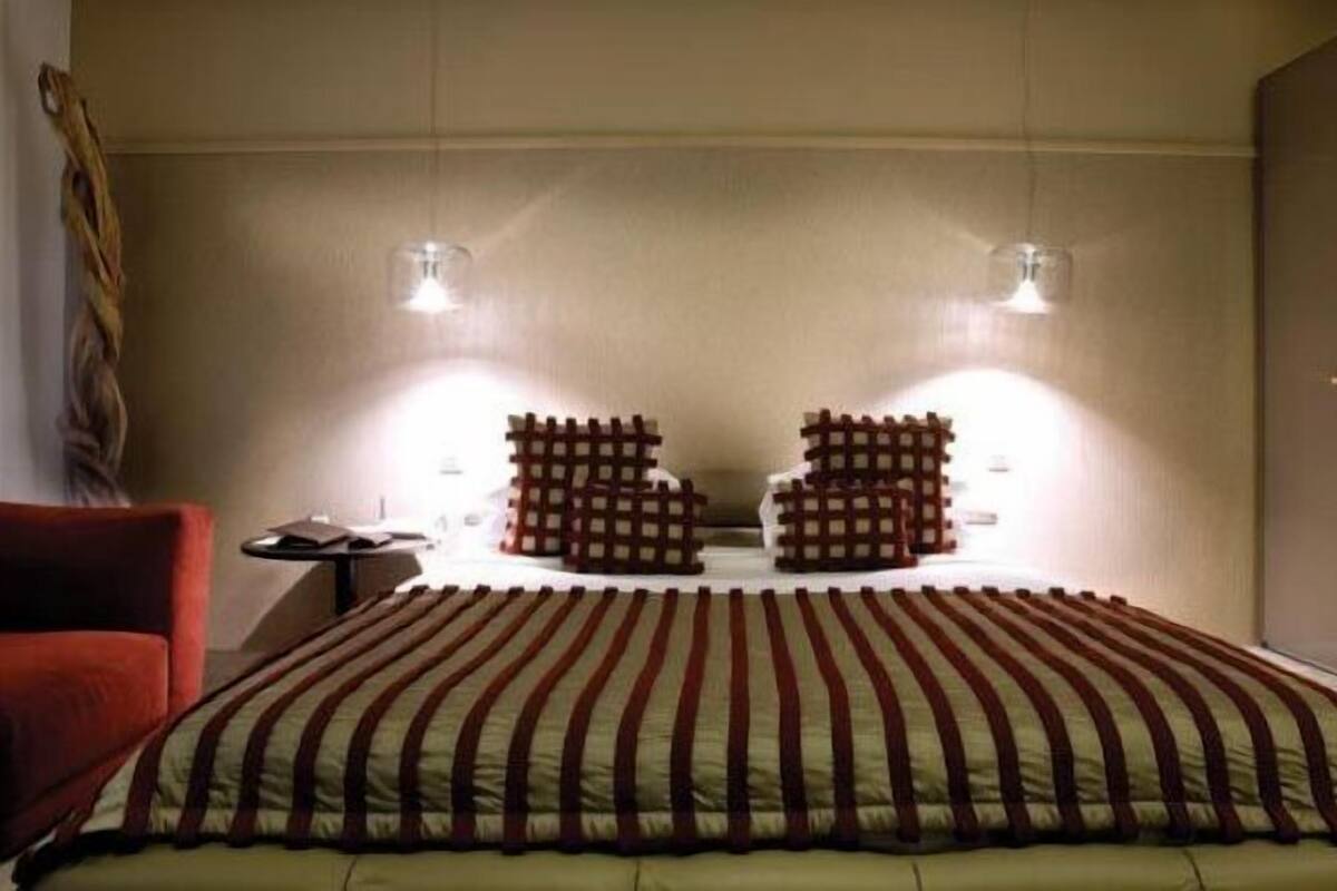 A bedroom with a large bed, two bedside tables, a red chair, and a wardrobe.