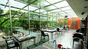 A restaurant with a glass enclosure, tables set with cutlery, and chairs. - The Park Pod (Chennai)