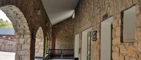 A corridor with stone walls, a tiled floor, and doors with green frames.