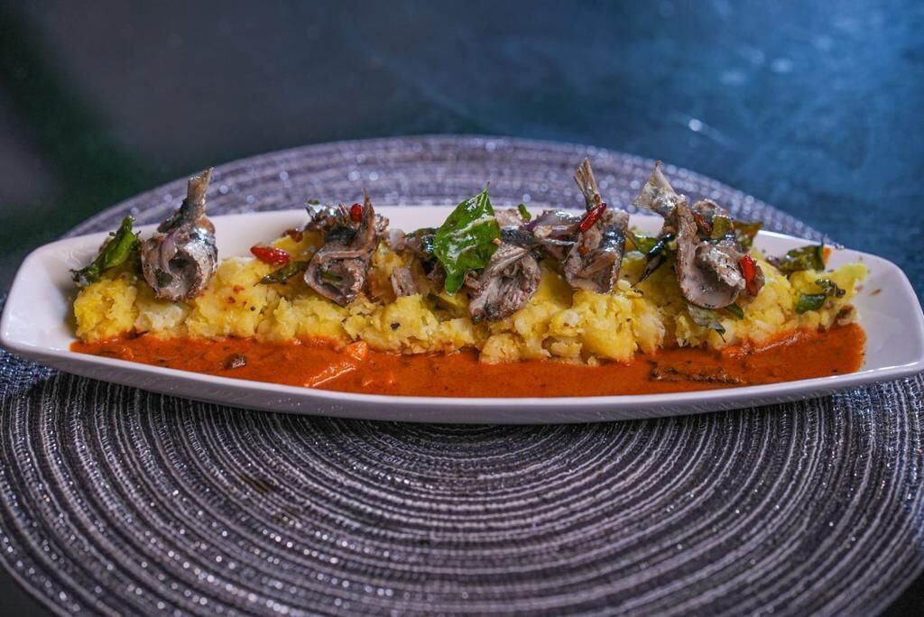 Un plato de comida con salsa roja, adornado con vegetales verdes y pescado.