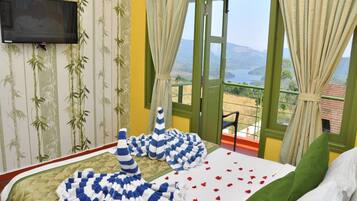 A hotel room with a bed, a TV, a balcony with a view of the mountains, and a window with curtains.