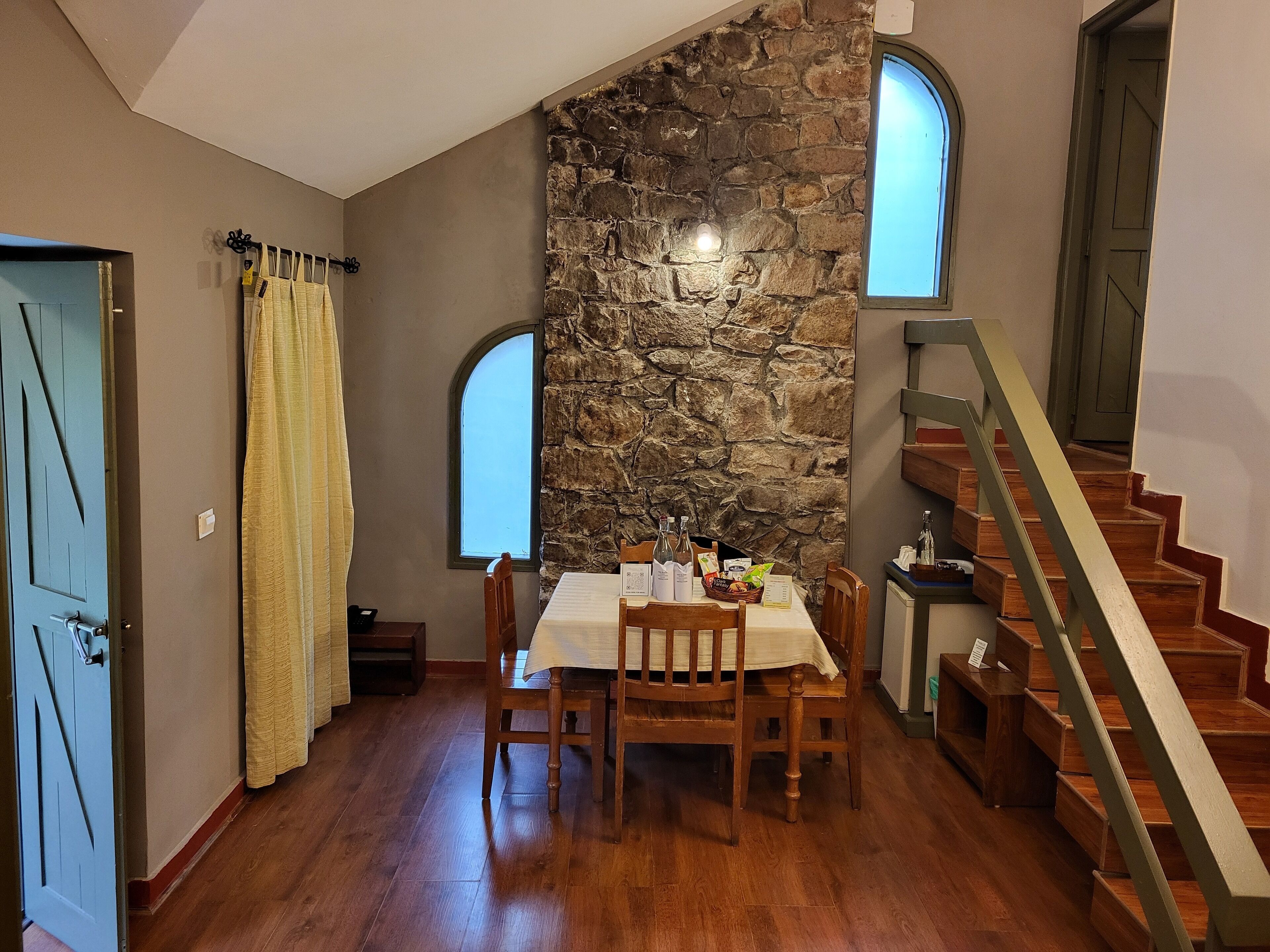 Un coin repas avec un mur en pierre, une table en bois, des chaises et un escalier.