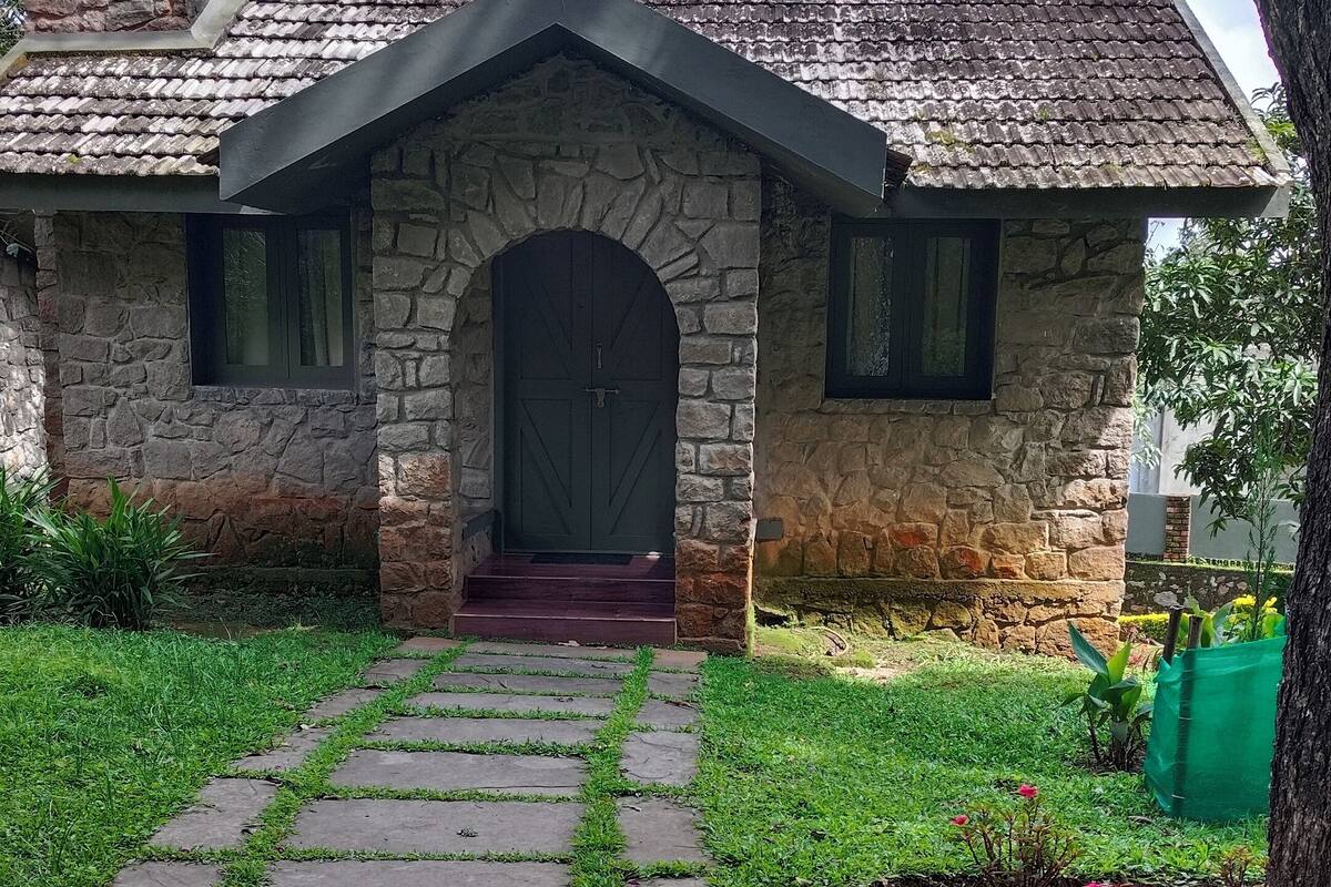 Uma casa de pedra com telhado de telhas, uma entrada em arco de pedra e um caminho pavimentado que leva à porta.