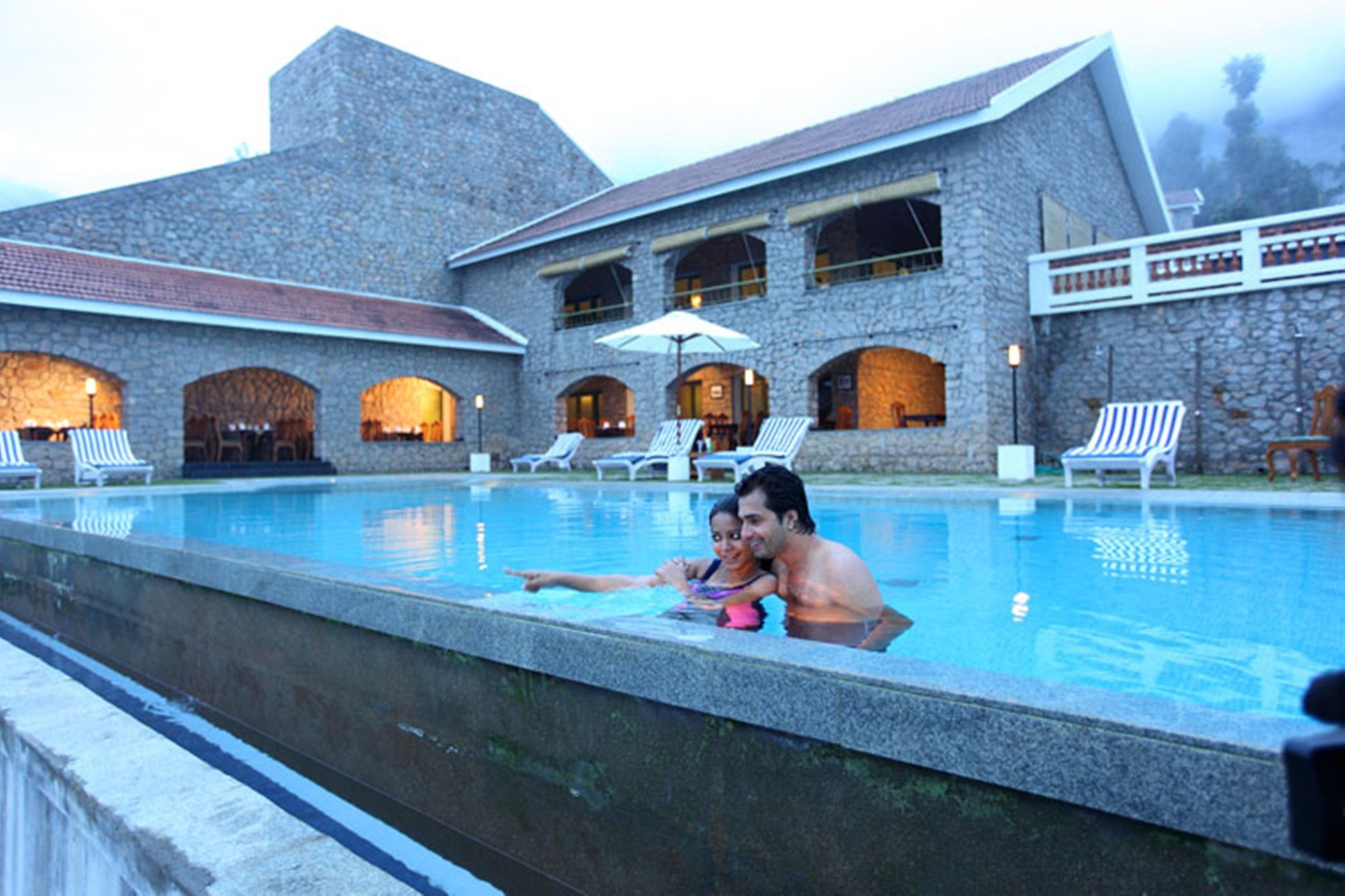 A pool area with lounge chairs and umbrellas, surrounded by stone buildings with arched windows.