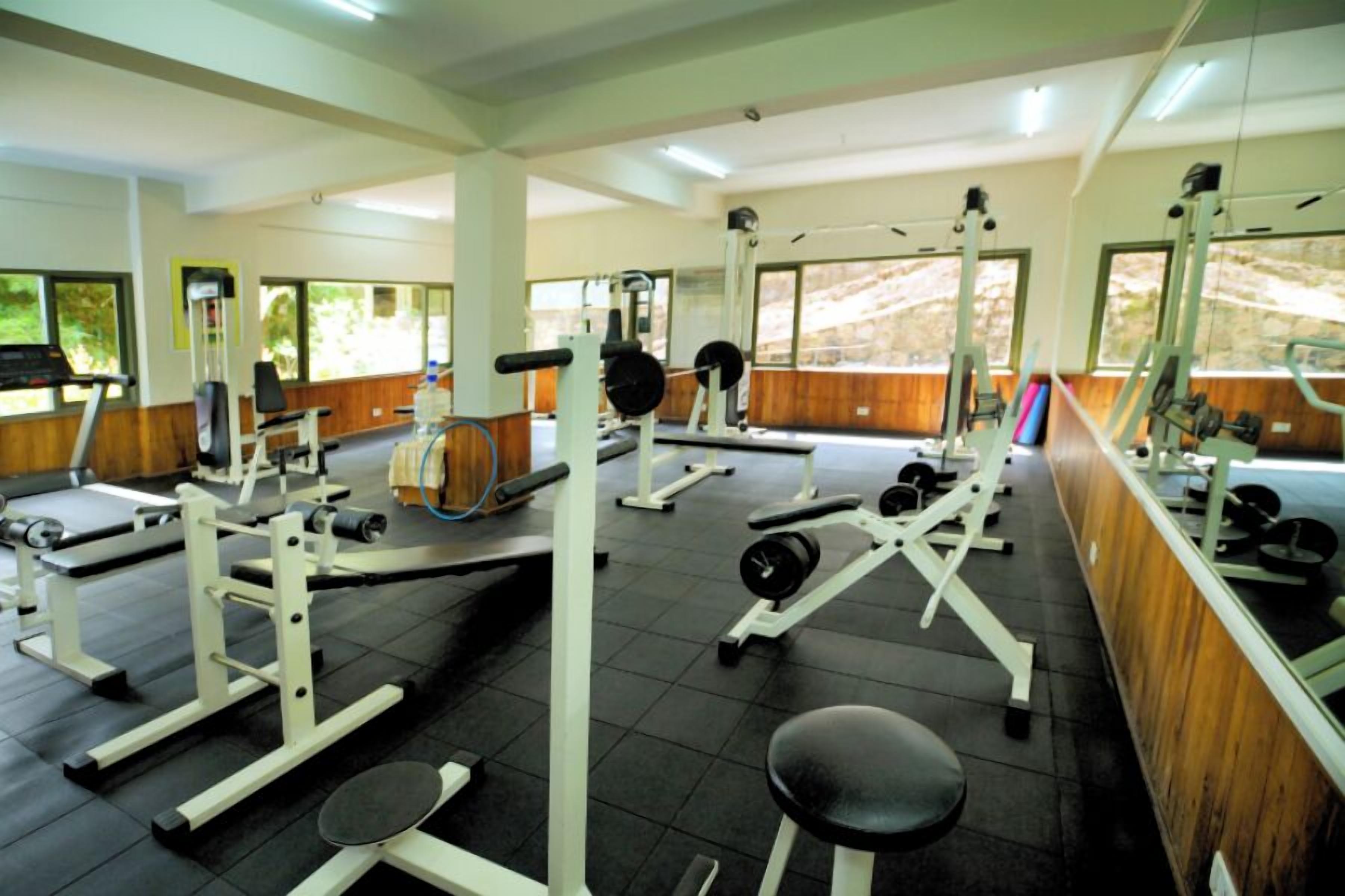 A gym with various exercise equipment, large windows, and a wooden wall.