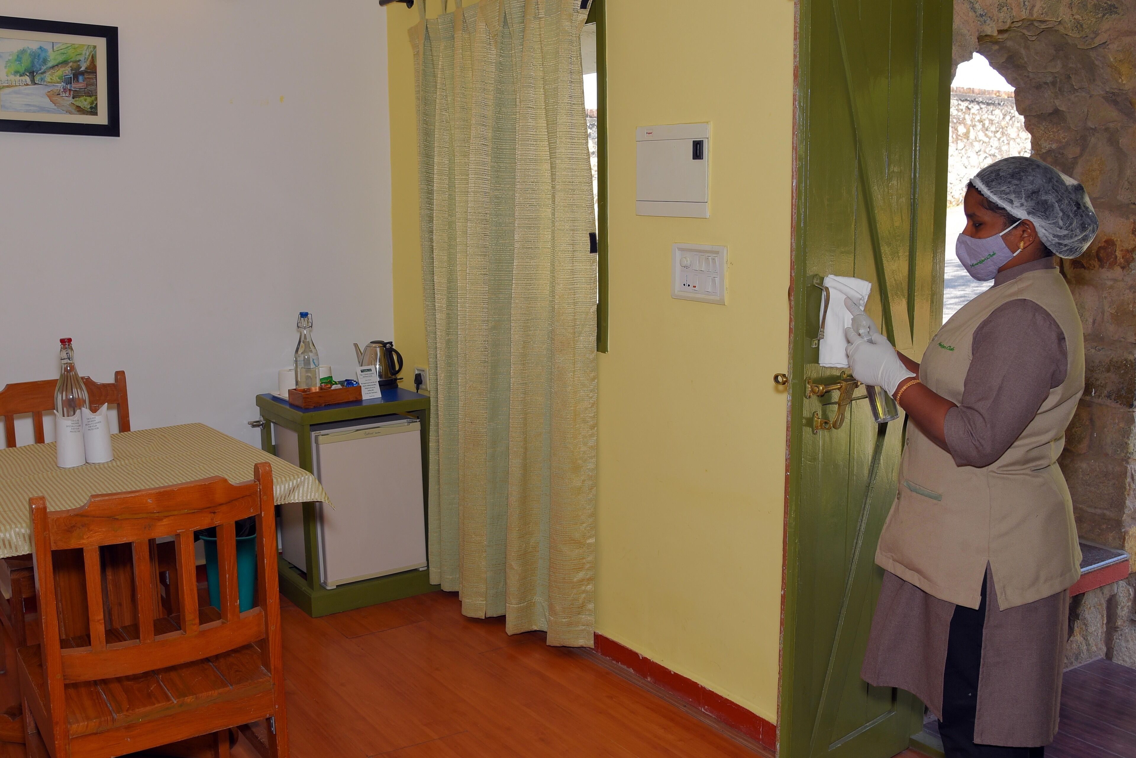 A room with a wooden table, chairs, a small refrigerator, and a green door.