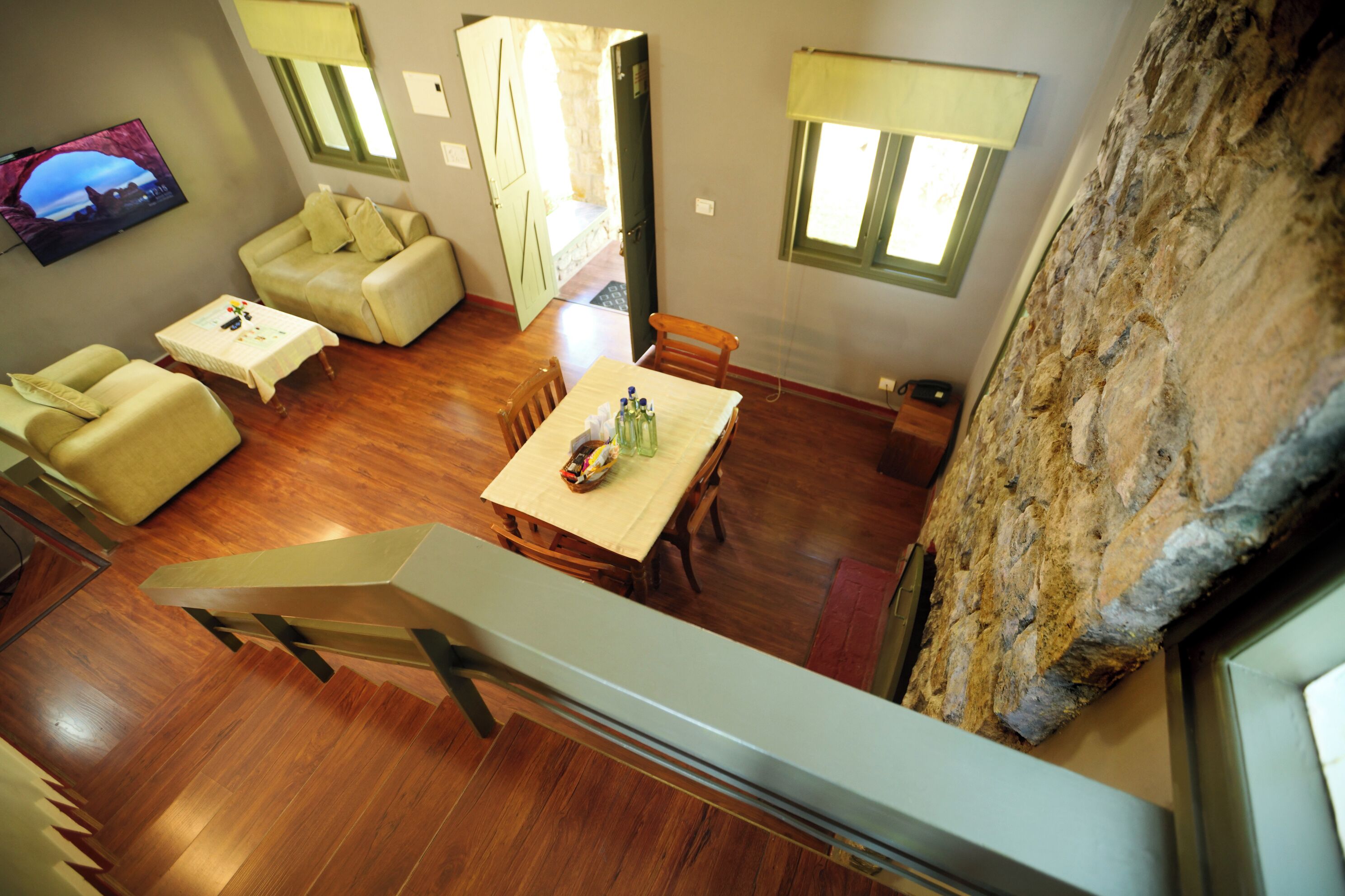 A spacious living area with a wooden floor, a dining table with chairs, a sofa, and a television mounted on the wall.