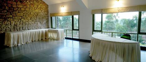 A spacious room with a stone wall, large windows, and a long table set for a meeting or event.