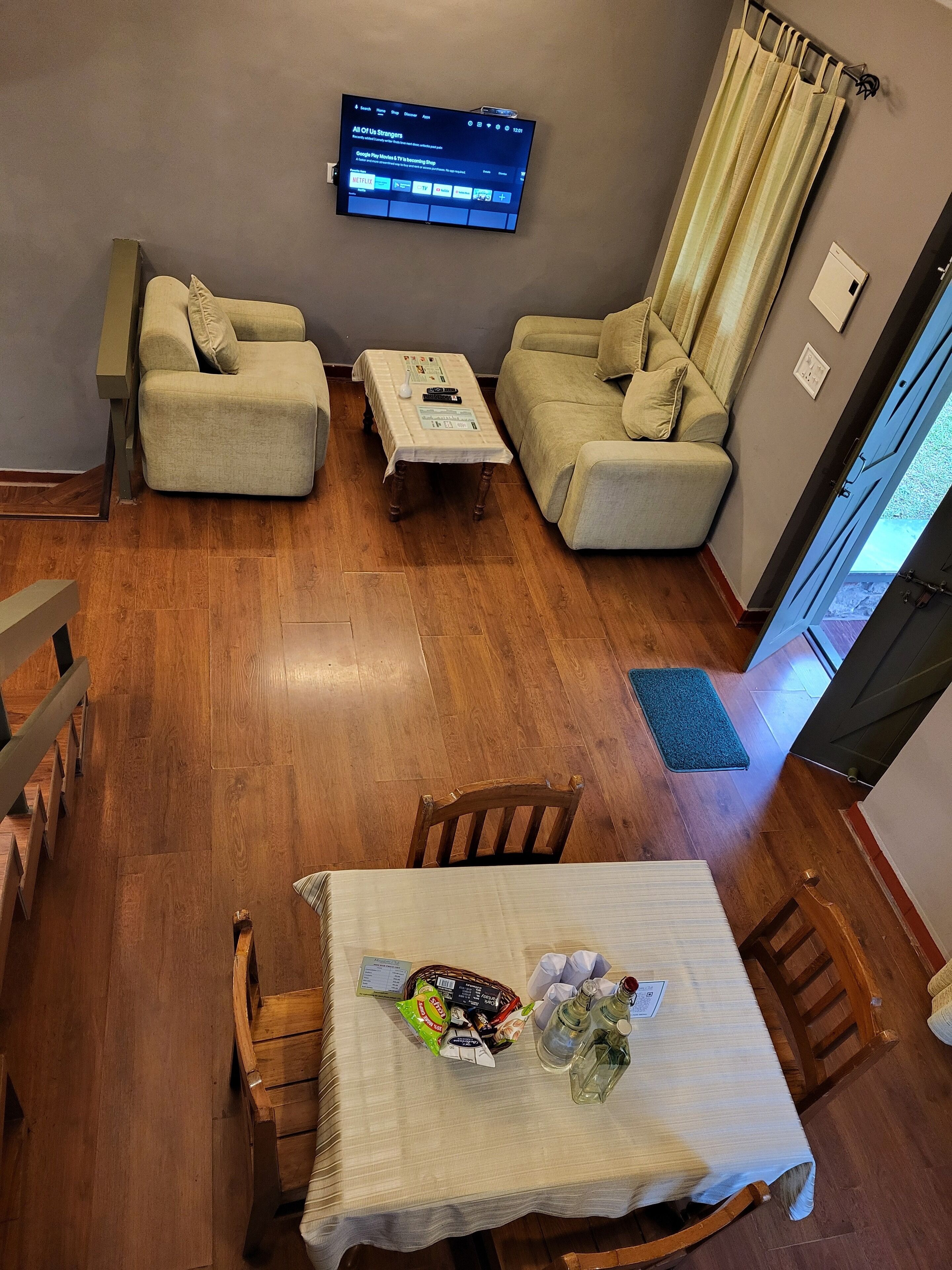 Una sala de estar con un televisor montado en la pared, dos sofás, una mesa de centro y una mesa de comedor con aperitivos.