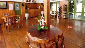 A wooden reception desk, a round wooden table with a floral centerpiece, and a seating area with chairs and a sofa.