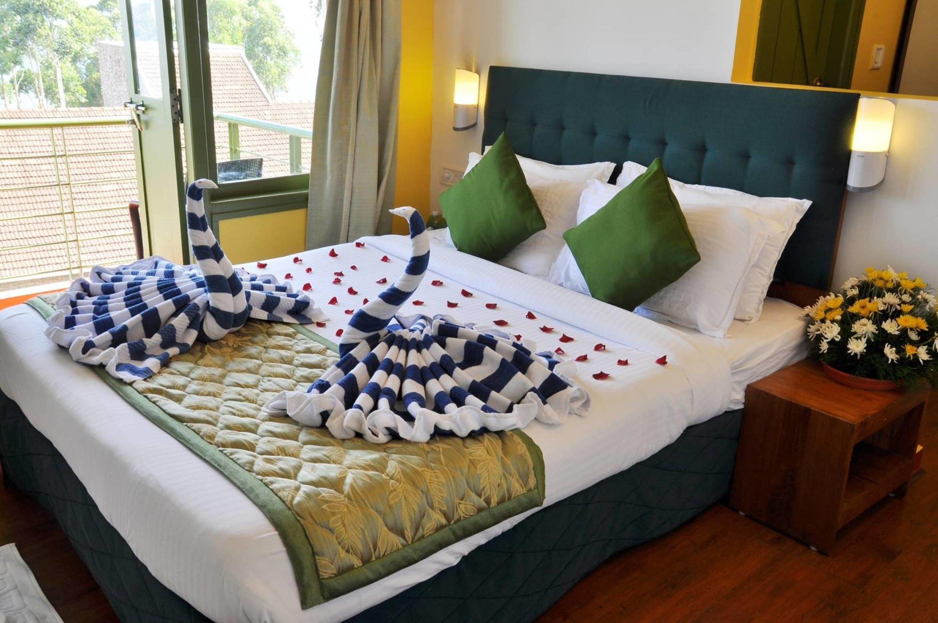 A neatly made bed with a striped blanket, green pillows, and a bouquet of flowers on a wooden nightstand.