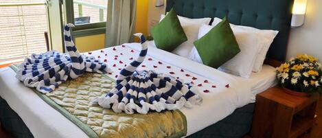 A neatly made bed with a striped blanket, green pillows, and a bouquet of flowers on a wooden nightstand.