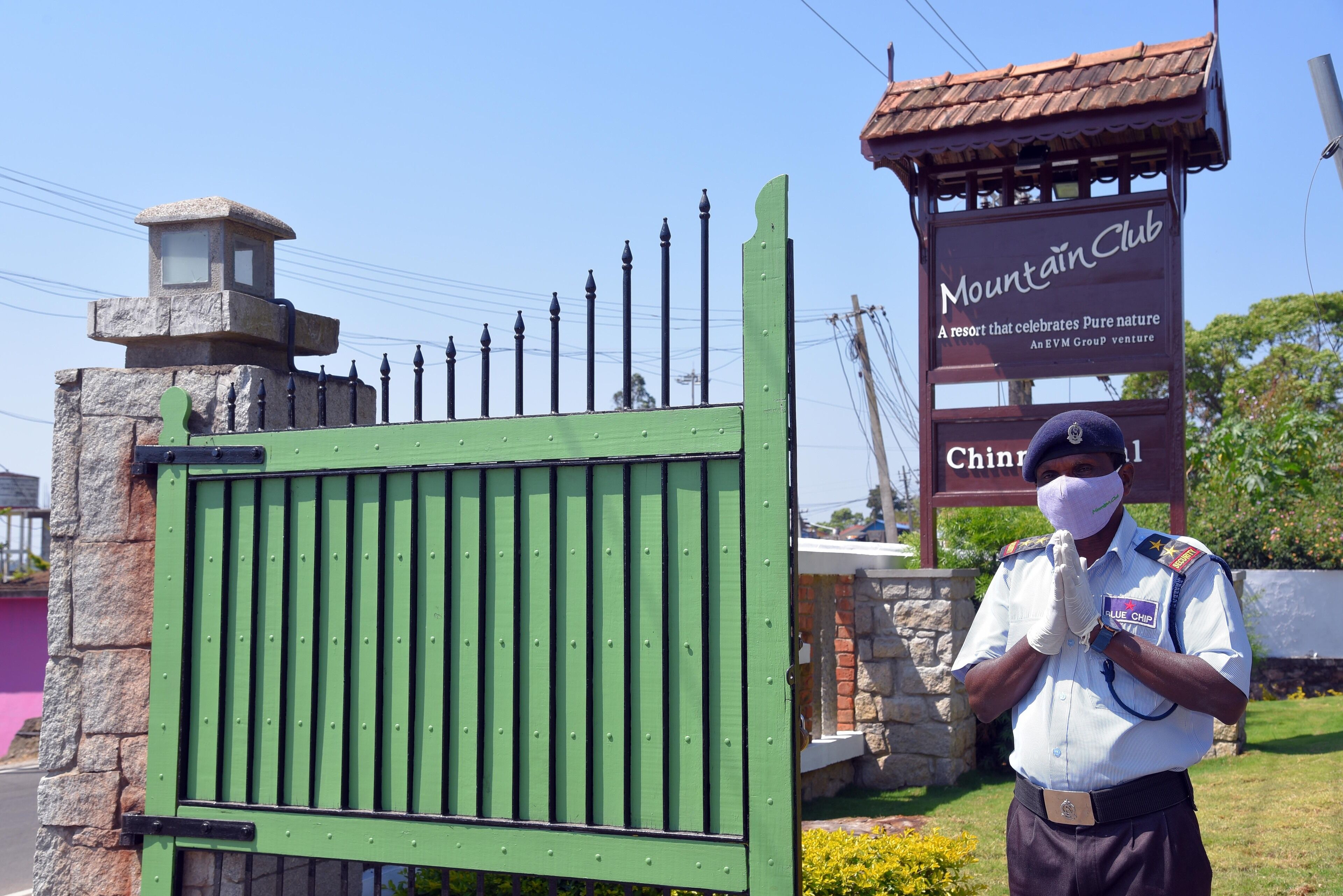 A security guard standing in front of a green gate with a sign that reads "Mountain Club."