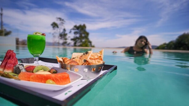 A tray with a variety of fruits and a green drink on a poolside table.