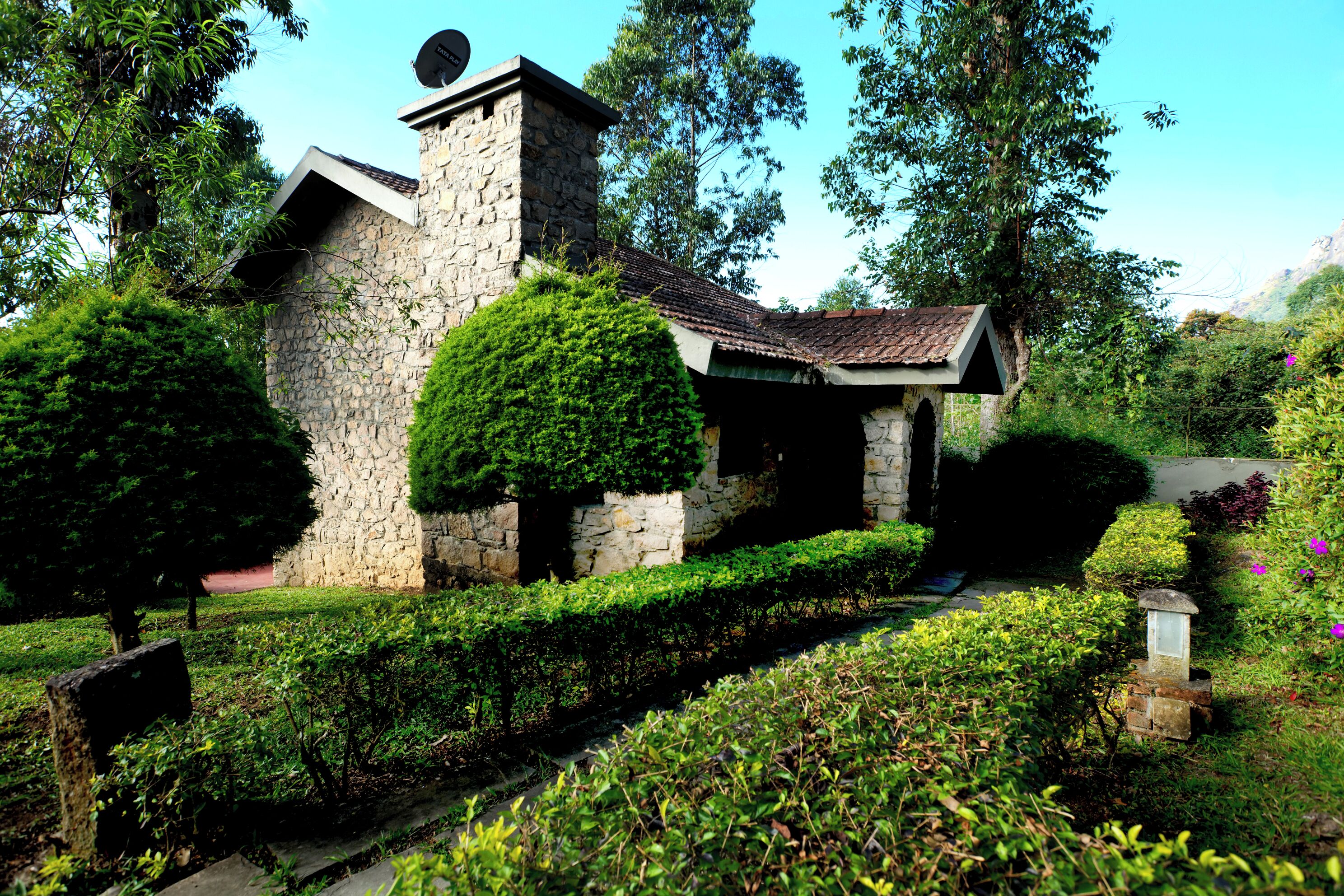 A stone building with a tiled roof, surrounded by well-maintained hedges and trees.