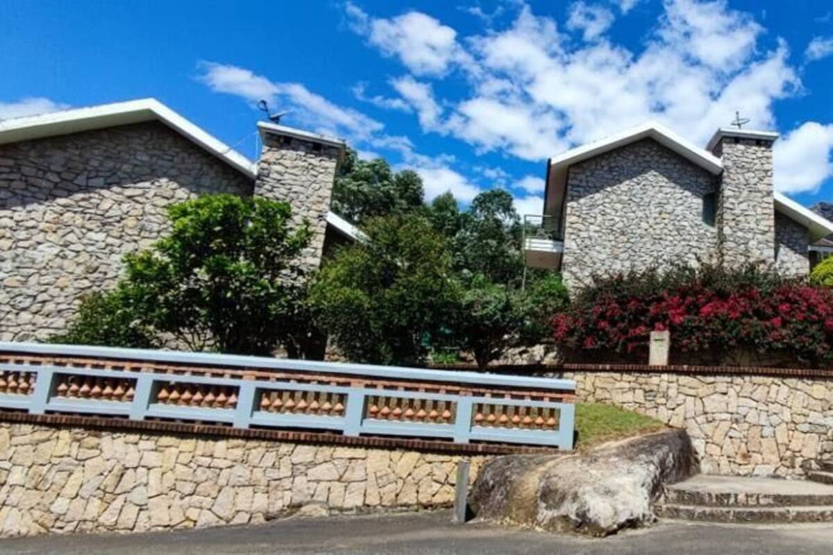 Um edifício de pedra com escadaria que leva a um portão, rodeado por vegetação e céu claro.