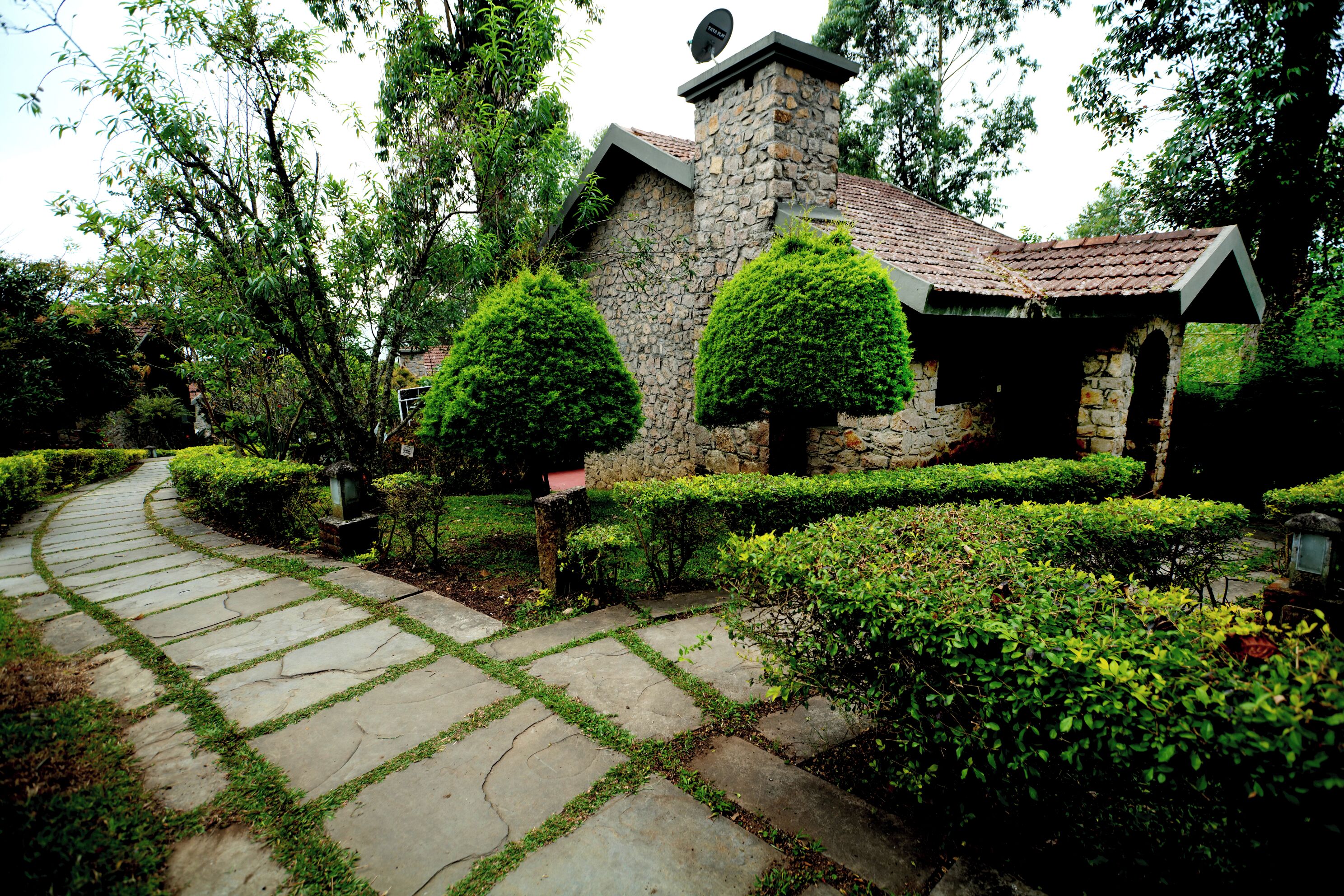 A stone house with a tiled roof, surrounded by well-maintained hedges and a stone pathway.