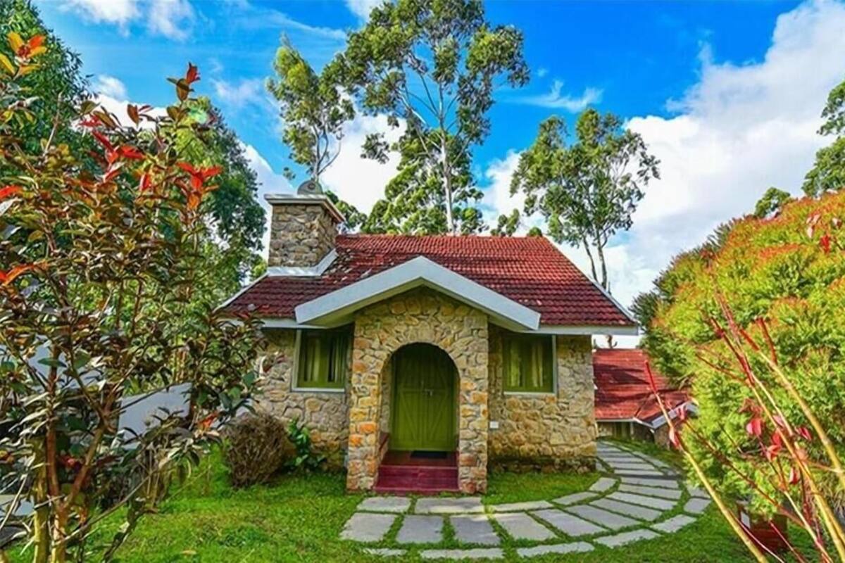 Uma casa de pedra com telhado de telhas vermelhas, porta verde e chaminé de pedra.