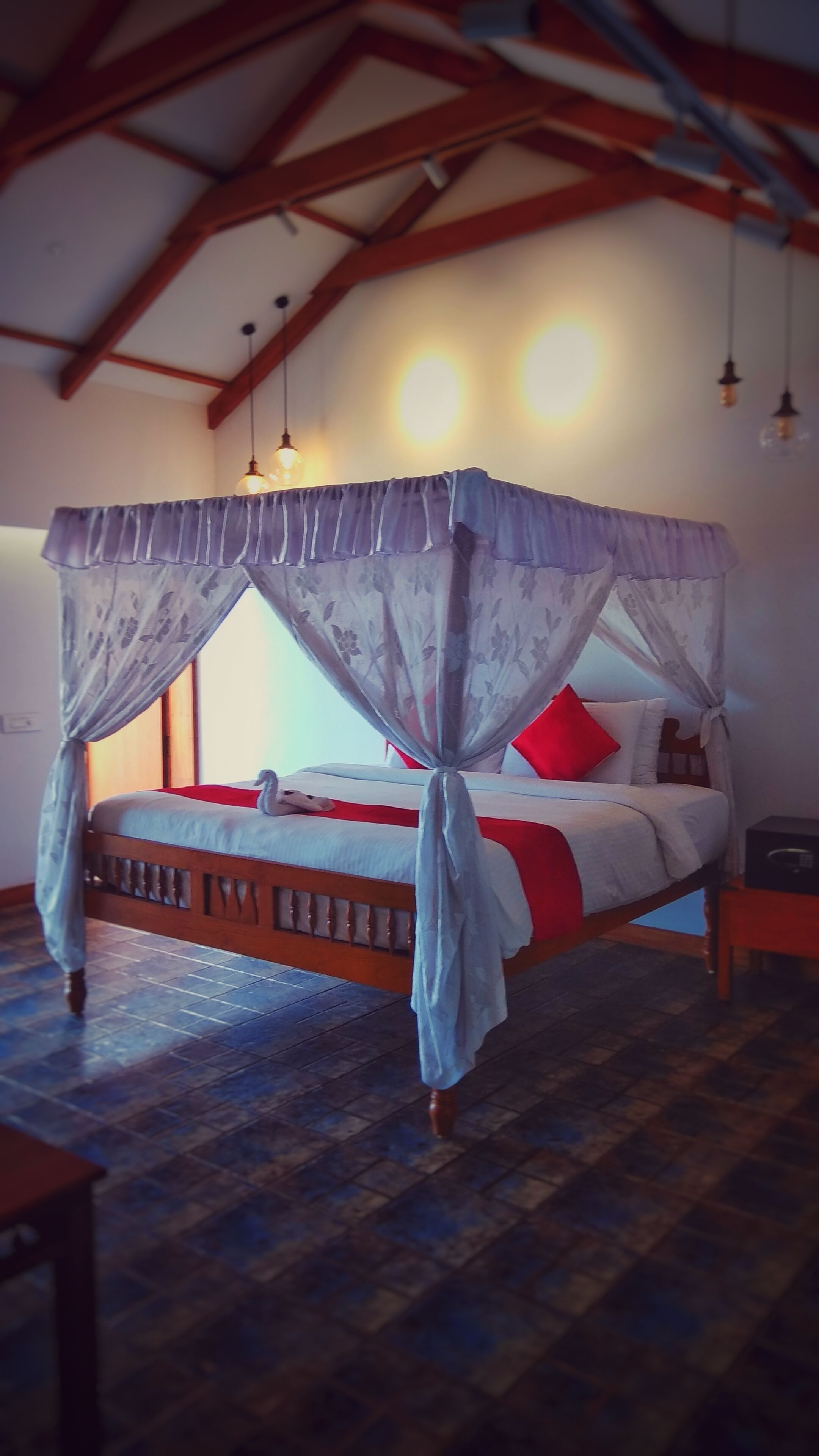 Una cama con dosel y cuatro columnas, con un cojín rojo, un cabecero de madera y una alfombra azul estampada.