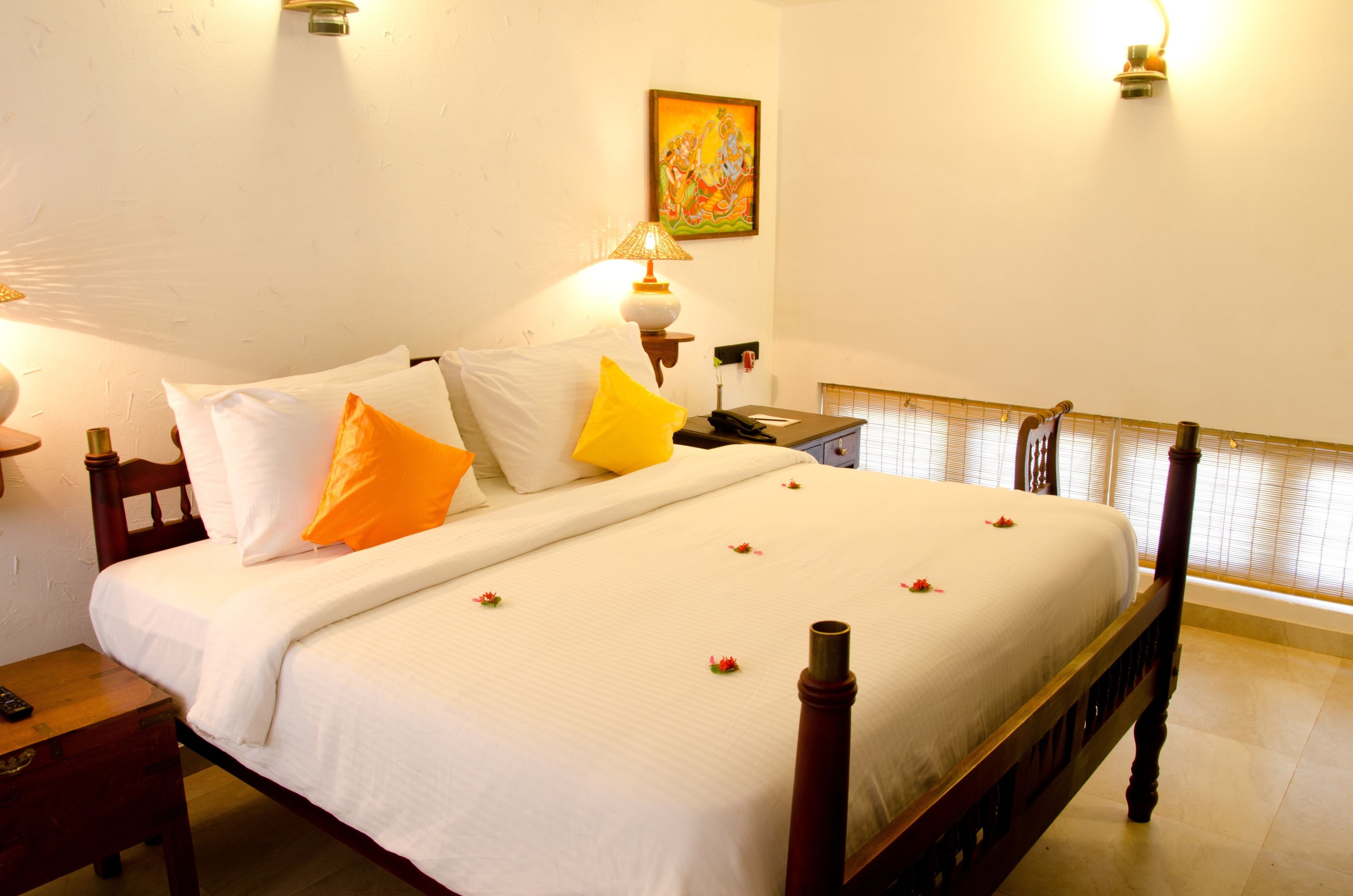 A neatly made bed with white and yellow pillows, a bedside table with a lamp, and a painting on the wall.