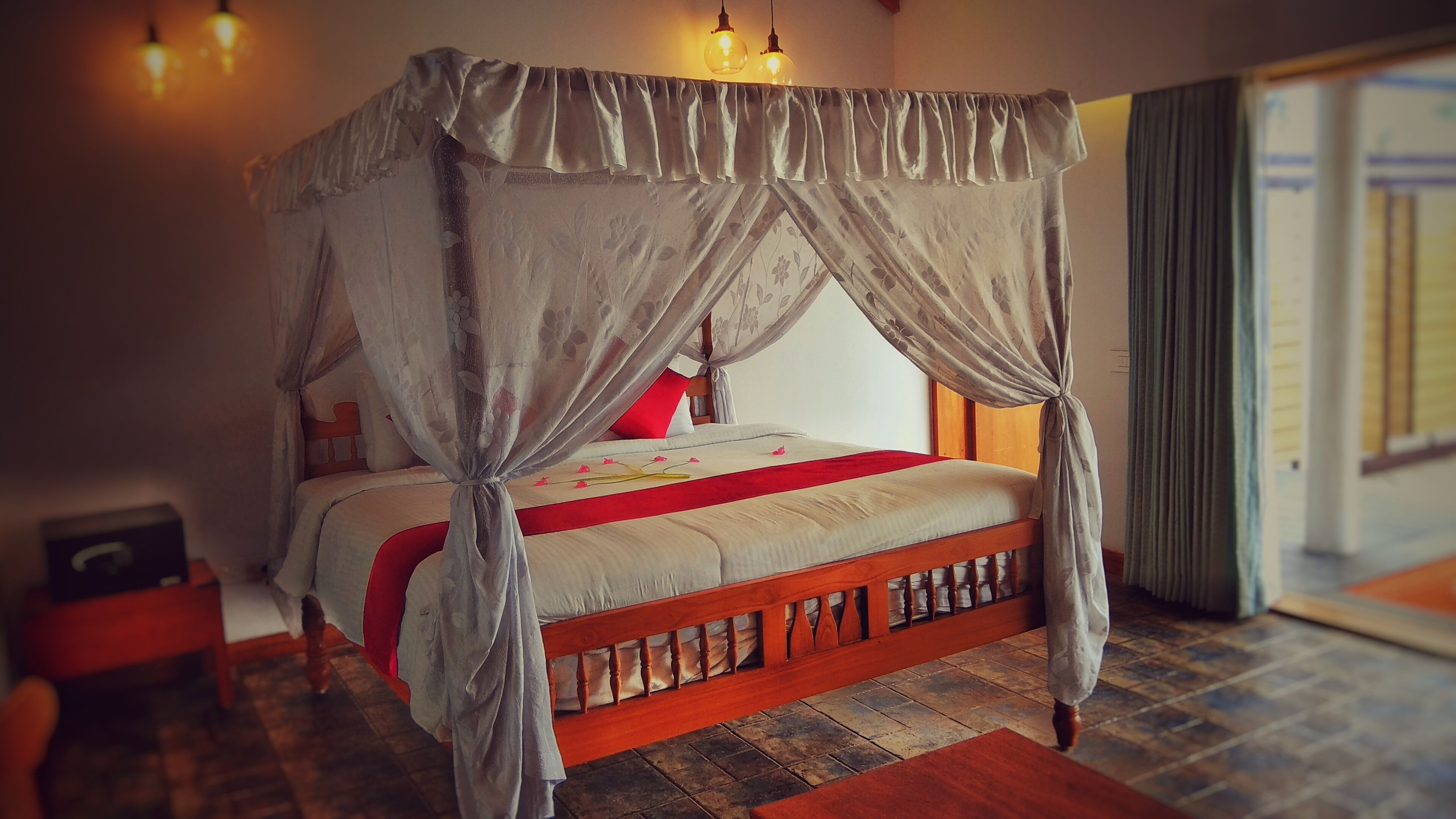 A four-poster bed with a canopy, wooden headboard, and a red accent pillow.