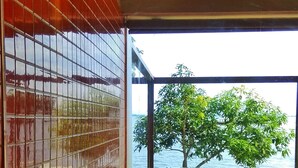 A modern bathroom with a glass-enclosed shower, a view of a tree and water body outside. - Punnamada Resorts (Ambalapuzha)