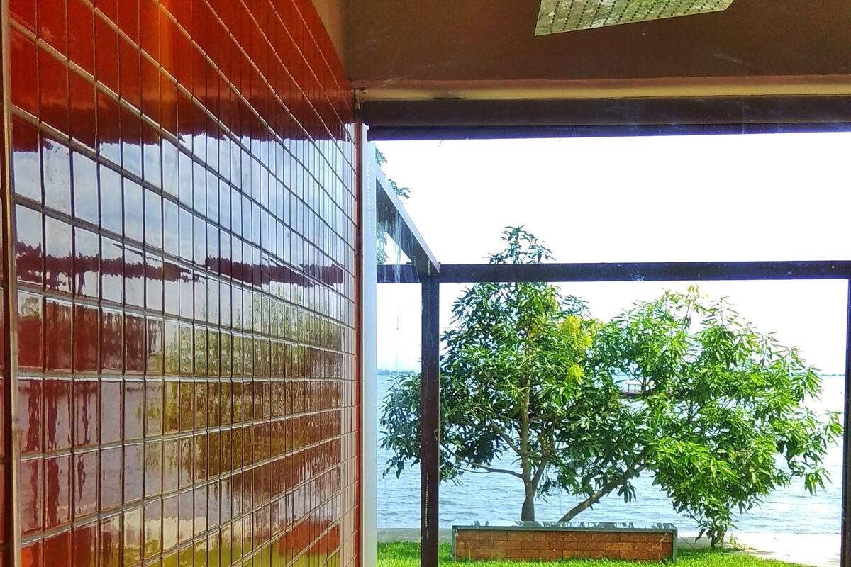 A modern bathroom with a glass-enclosed shower, a view of a tree and water body outside.