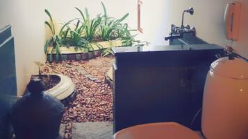 A small bathroom with a toilet, sink, and a window with blinds. There are plants and a decorative item on the floor.