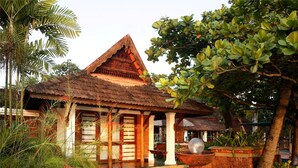 A traditional house with a tiled roof, surrounded by lush greenery and a paved walkway. - Punnamada Resorts (Ambalapuzha)