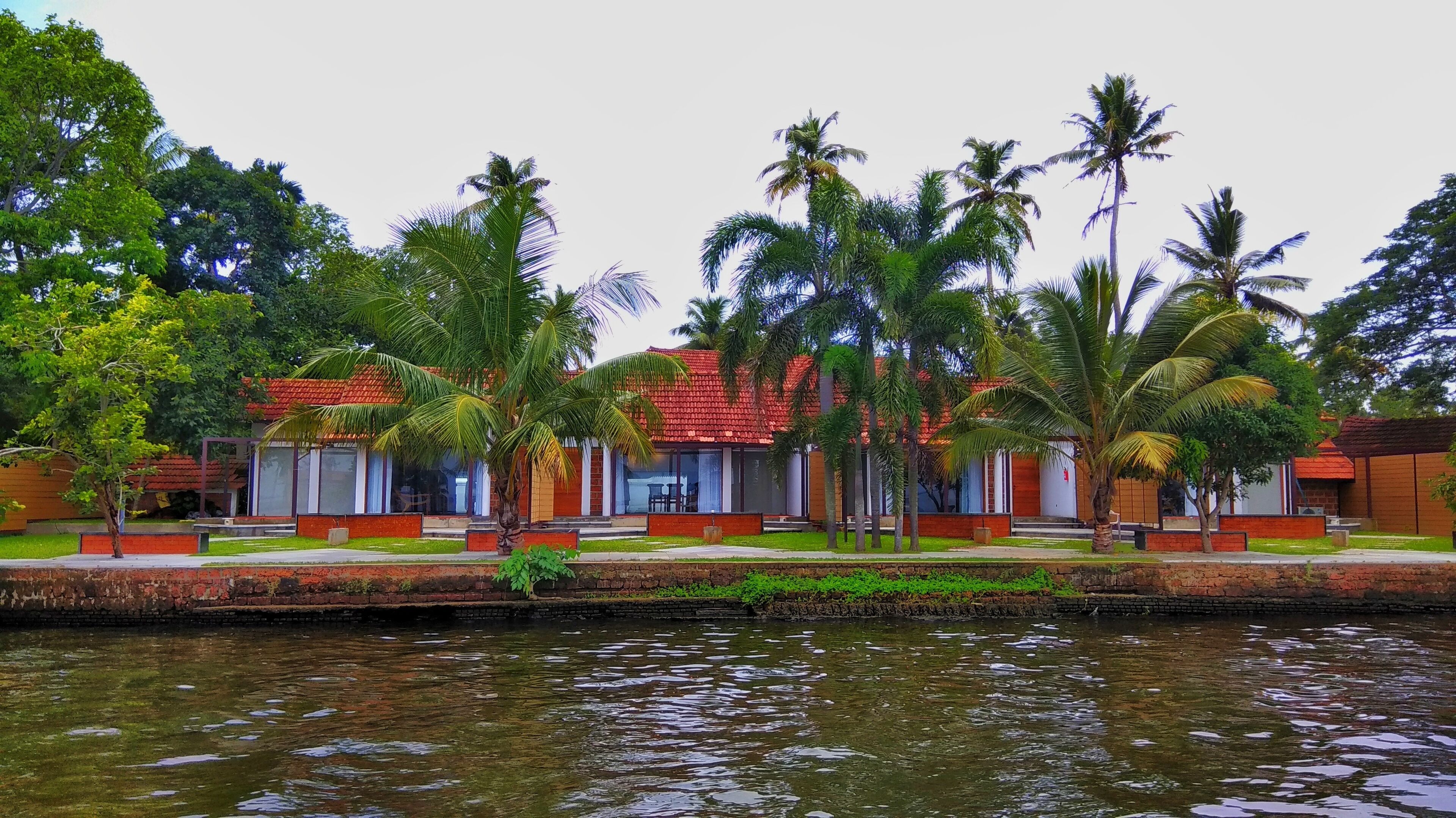 A riverside hotel with multiple rooms, palm trees, and a calm water body.