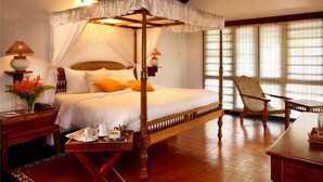 A four-poster bed with a canopy, a wooden nightstand with a lamp, a chair, and a table with a tray of breakfast items. - Punnamada Resorts (Ambalapuzha)