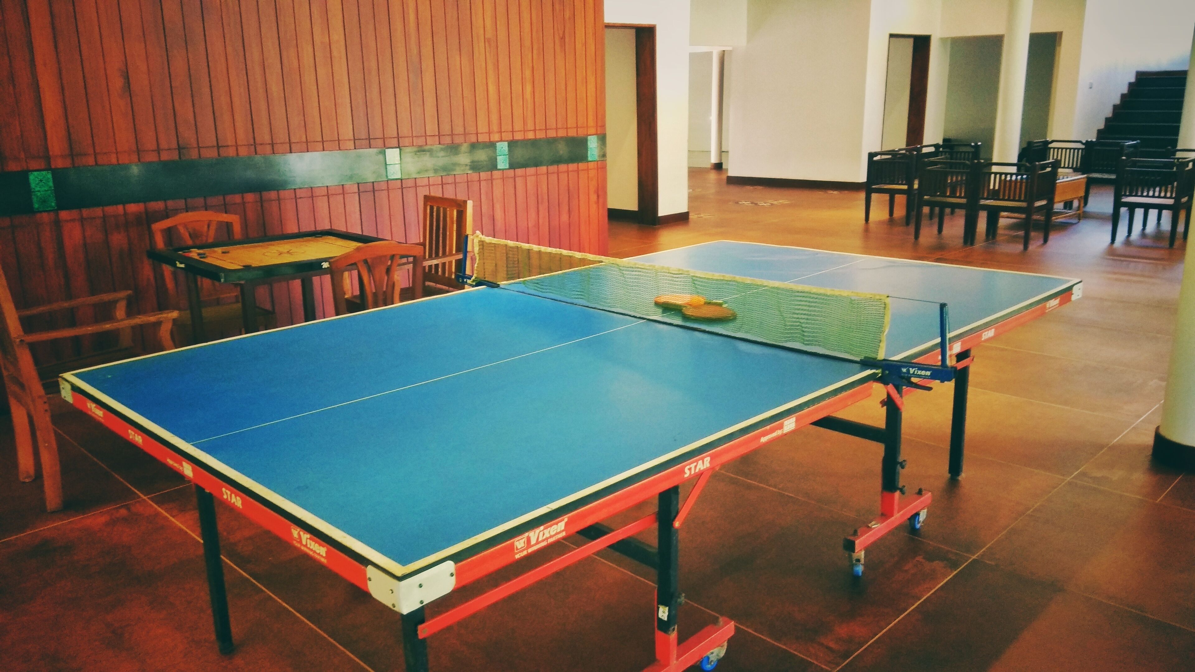 A ping pong table in a room with wooden paneling and chairs.
