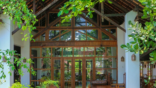 A wooden structure with large glass windows and a covered patio area with furniture. - Punnamada Resorts (Ambalapuzha)