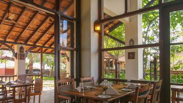 Un restaurante con mobiliario de madera, ventanas amplias y un techo de paja.
