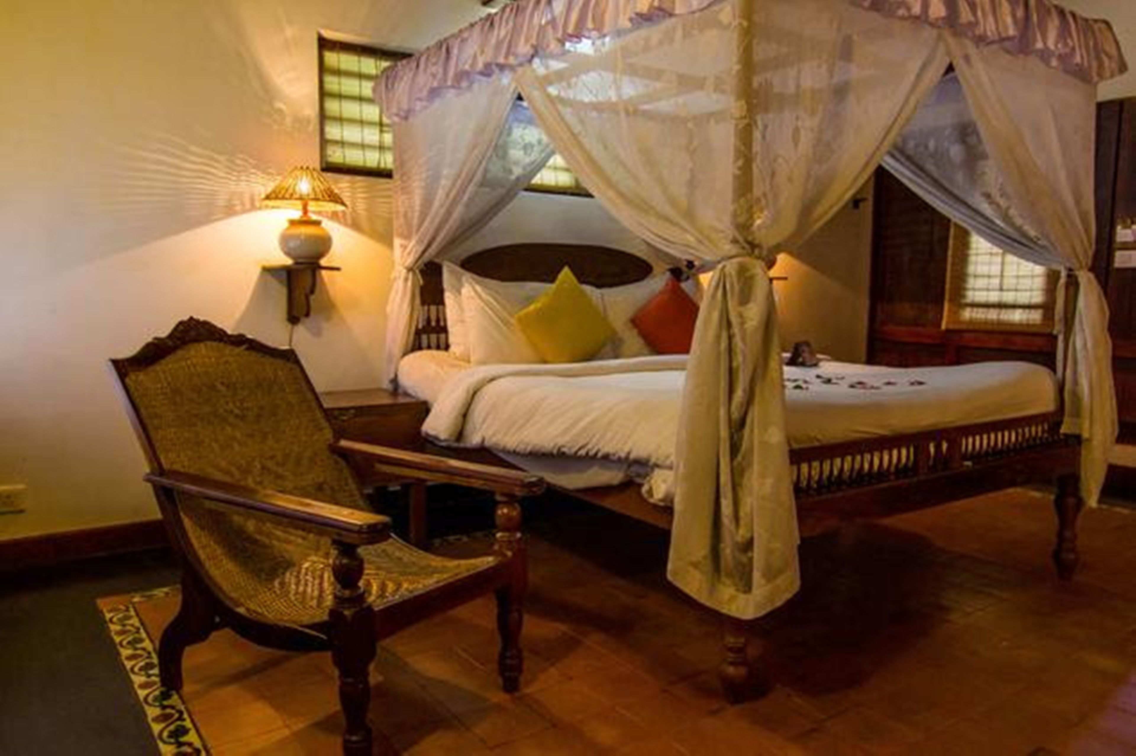 A four-poster canopy bed with a wooden frame, a chair, and a wall-mounted lamp.