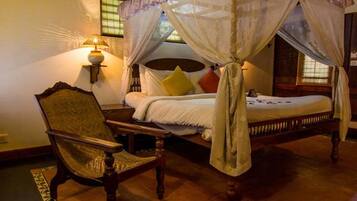 A four-poster canopy bed with a wooden frame, a chair, and a wall-mounted lamp.