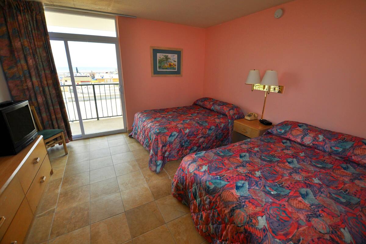 A hotel room with two beds, a television, a sliding door to a balcony, and a painting on the wall.