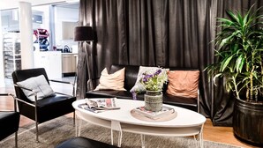 A modern living room with a black leather sofa, a white coffee table, and a large potted plant. - Hotell Mörby AB, Patienthotell (Danderyd)