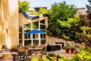 An outdoor patio area with wooden furniture, a blue umbrella, and potted plants. - Hotell Mörby AB, Patienthotell (Danderyd)