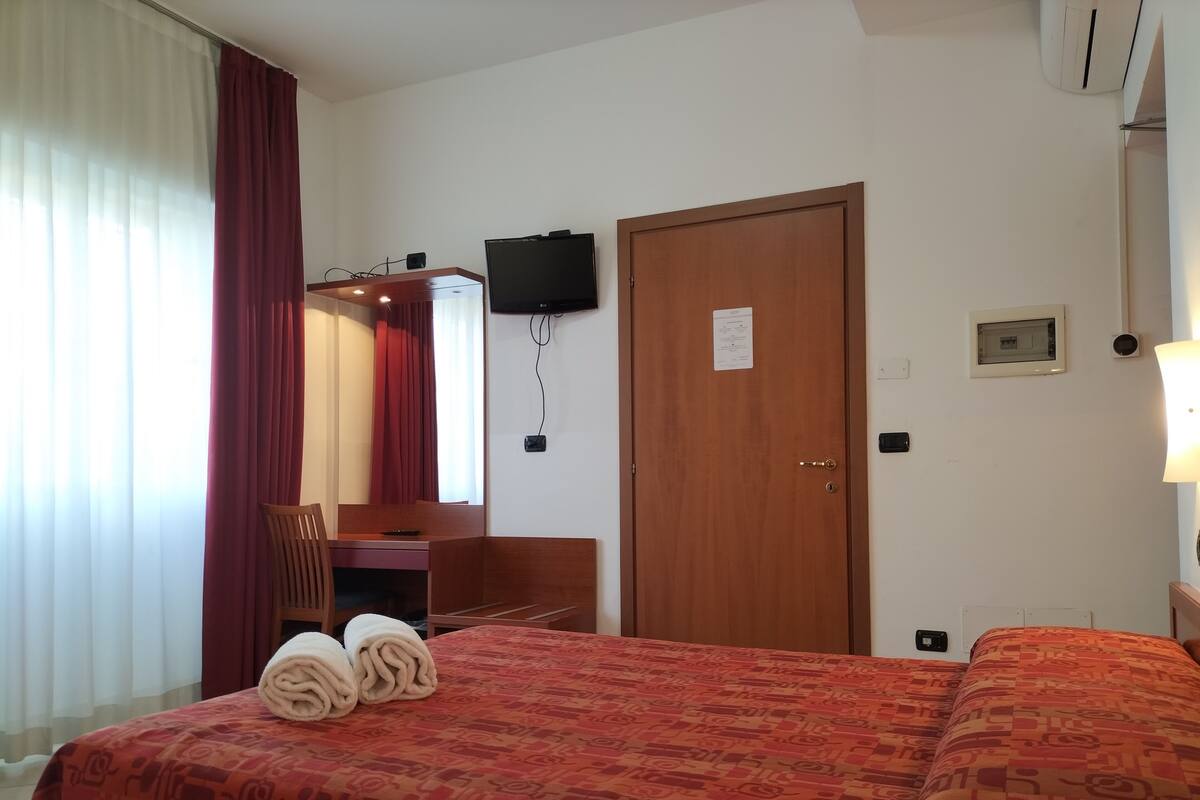 A hotel room with a bed, a desk, a chair, a television, and a door.