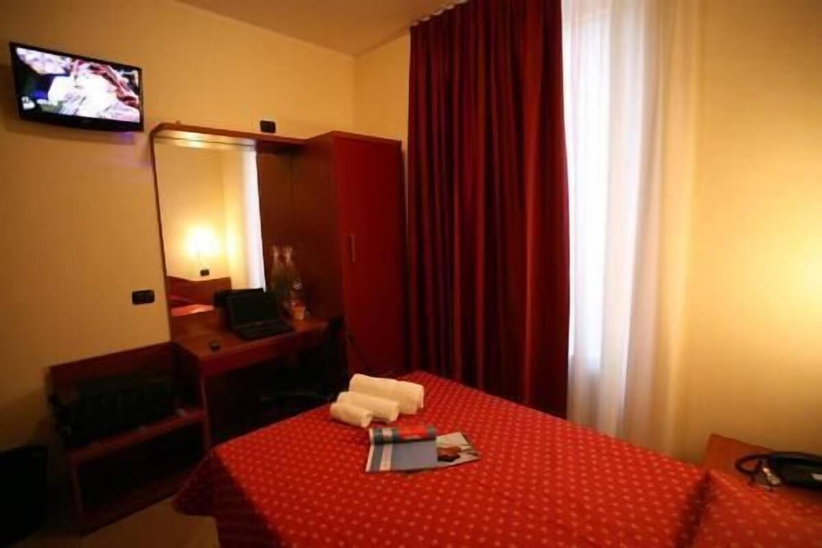 A hotel room with a bed, a desk, a chair, a television, and a mirror.