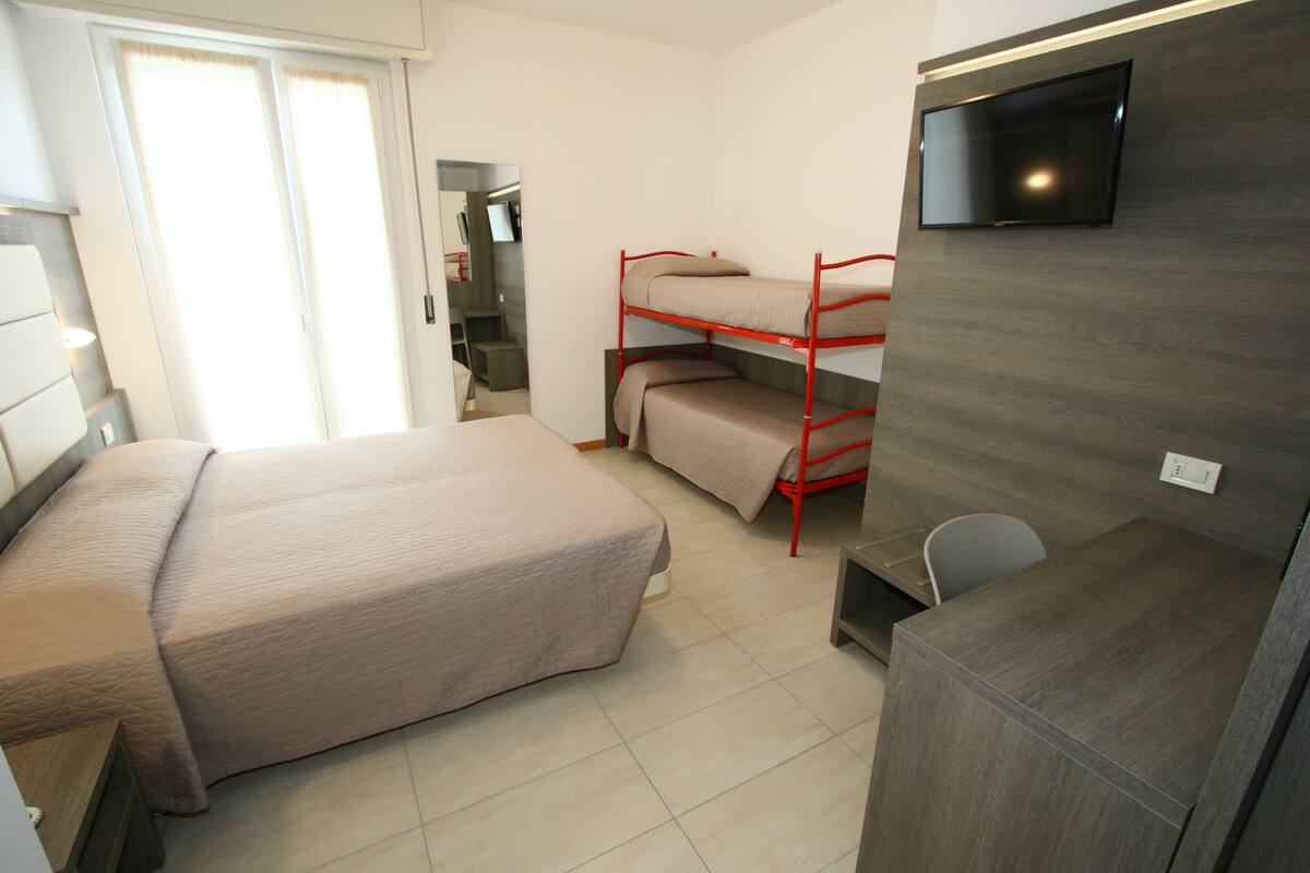 Une chambre d’hôtel avec un lit simple, un téléviseur fixé au mur et un lit superposé dans un coin.
