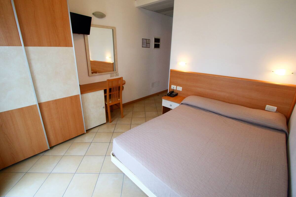 Une chambre à coucher avec un lit, une armoire en bois, un bureau avec une chaise et un miroir.