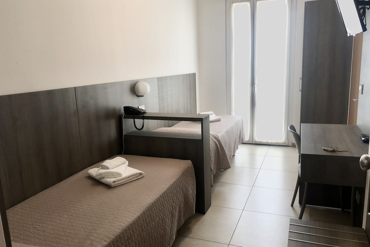 Une chambre avec deux lits, un bureau, une chaise, un téléphone et une grande fenêtre.