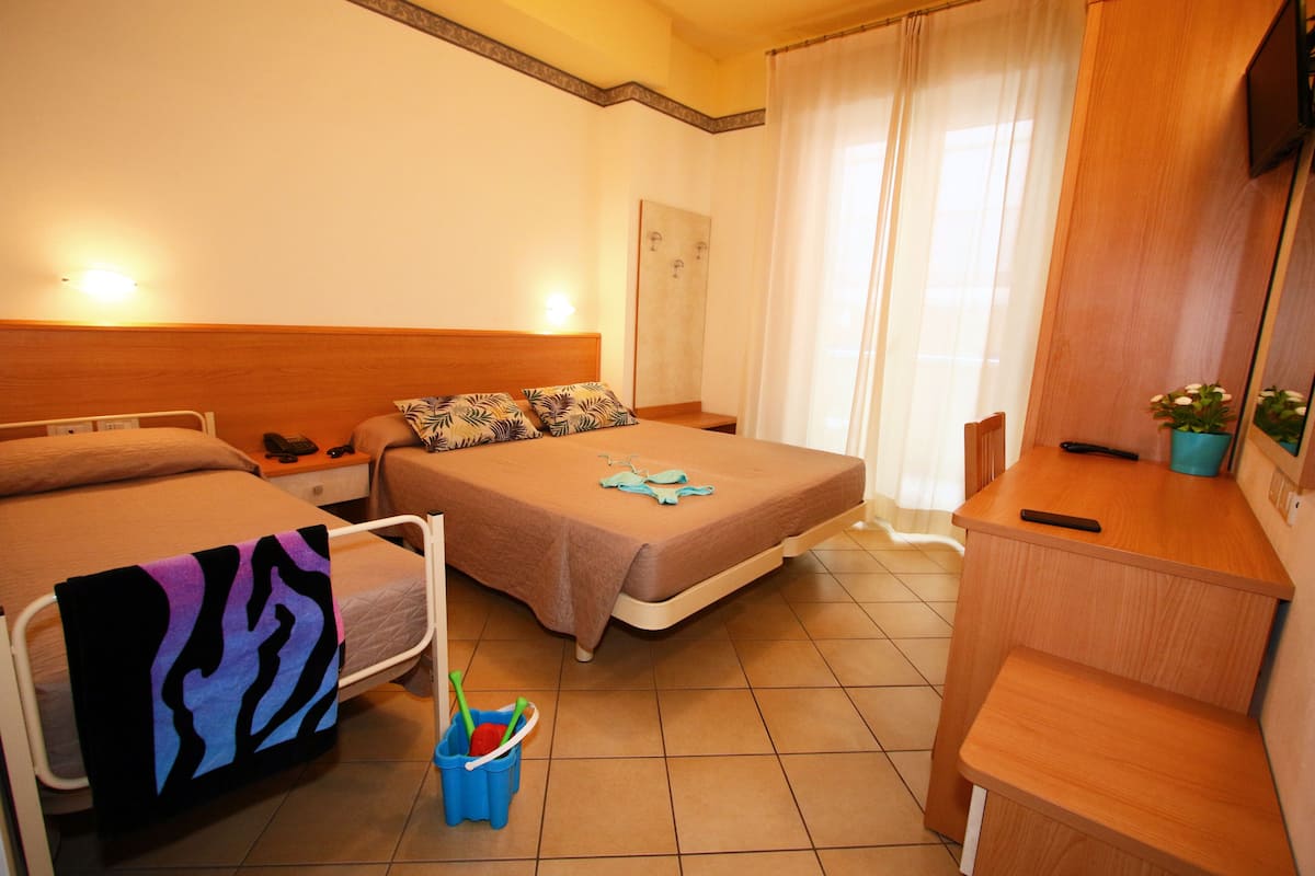 Une chambre d’hôtel avec deux lits, un bureau et une chaise. On y trouve une petite table avec une plante et un miroir.