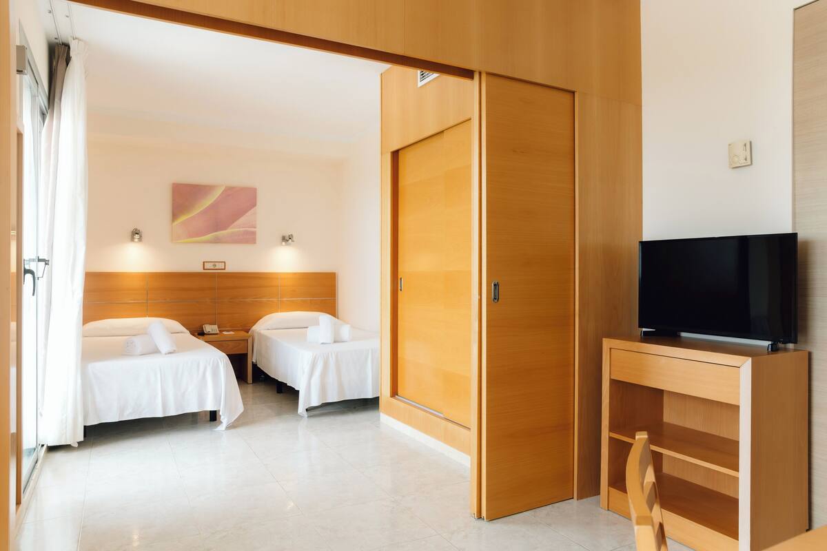 A hotel room with two beds, a TV, and a wooden wardrobe.