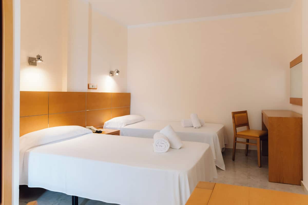 A hotel room with two beds, a desk, a chair, and a mirror.