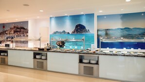 A buffet counter with a coastal mural, a microwave, and a variety of food items. - Bluesea Salina (Santa Eulalia del Rio)