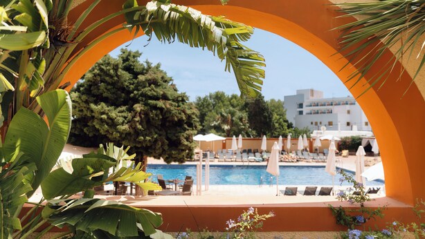 A pool area with lounge chairs and umbrellas, surrounded by greenery and a clear sky. - Bluesea Salina (Santa Eulalia del Rio)